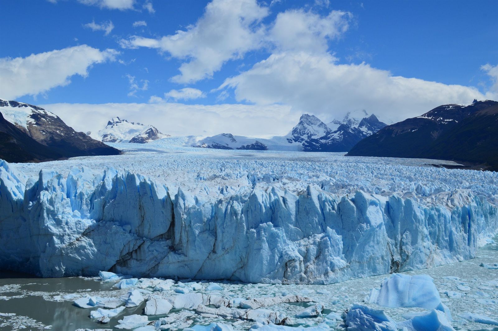 Wall of blue glacier ice meeting a lake below snowy Patagonian peaks